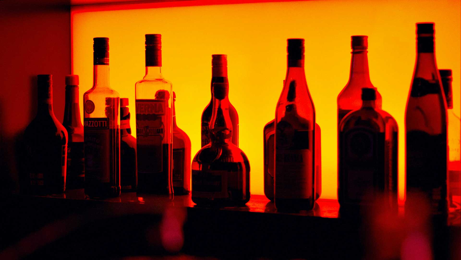 Alcohol bottles on a shelf lit from behind with an amber glow