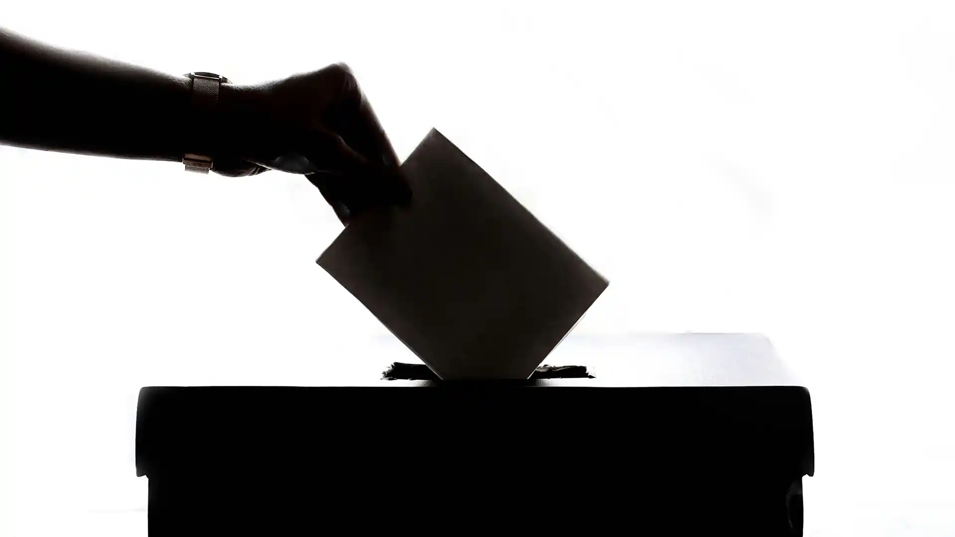 Silhouette of a hand dropping a ballot into a box.