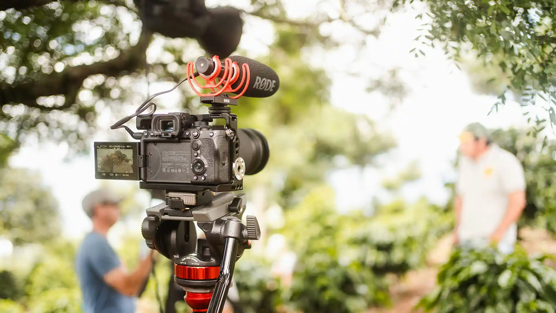 DSLR camera with a microphone attached at top filming a person in the background
