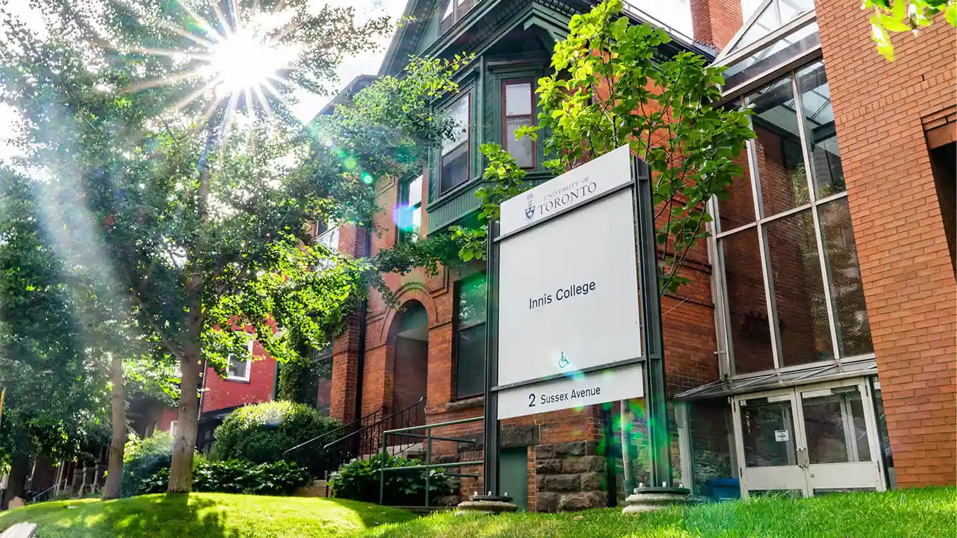 A Victorian-style building on a sunny day. A sign in front with the University of Toronto logo and the words Innis College, 2 Sussex Avenue in front.