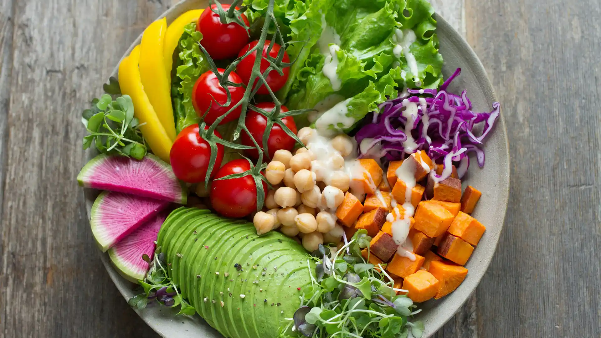 a bowl of fresh food including avocados, chickpeas, sweet potatoes, cherry tomatoes, cabbage, and lettuce