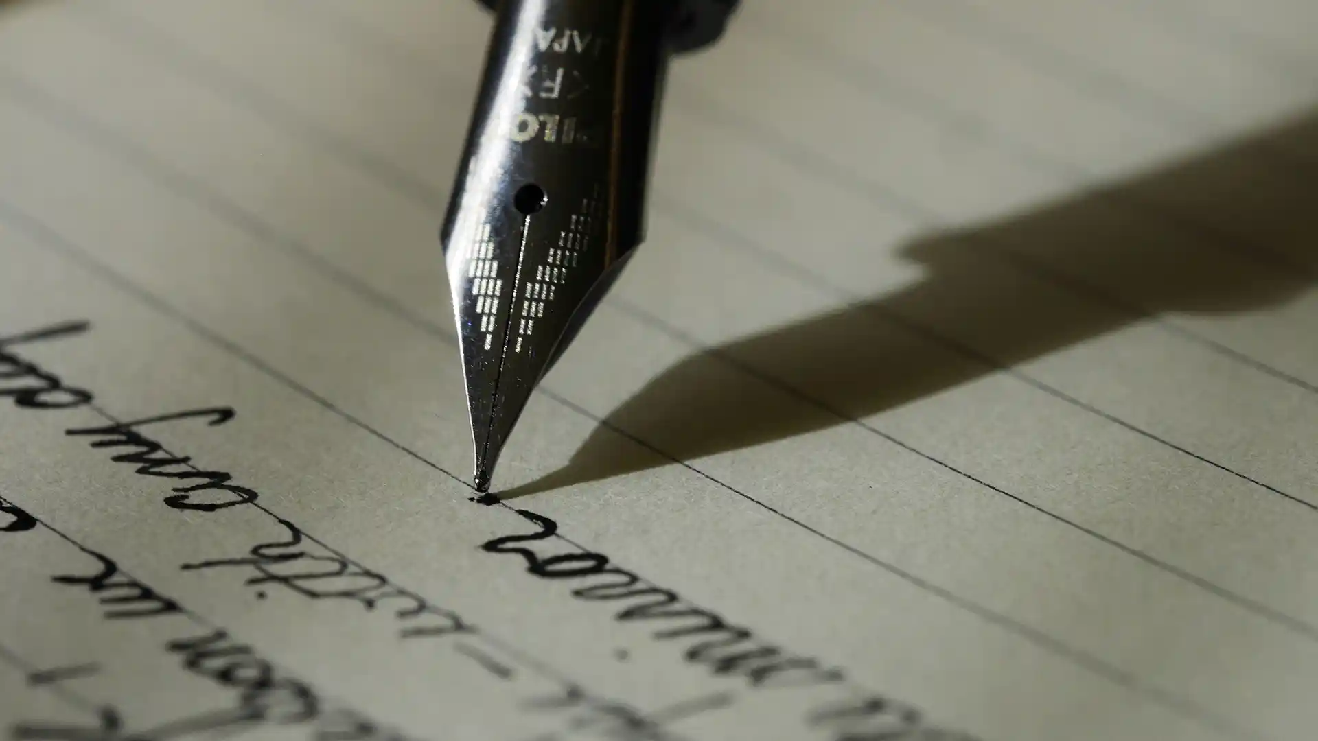 Close up of an ink well pen writing in cursive on a piece of lined paper