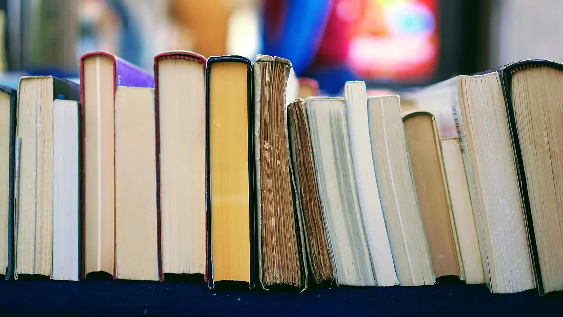 A stack of books, all different sizes, lined up on a shelf