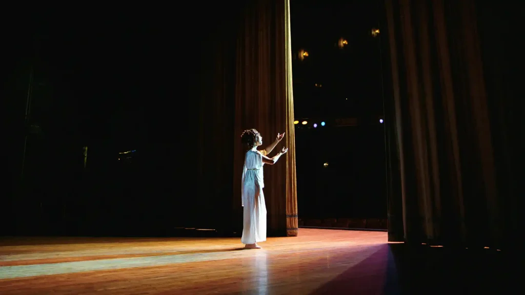 An opera singer in a white Grecian dress singing out towards the audience